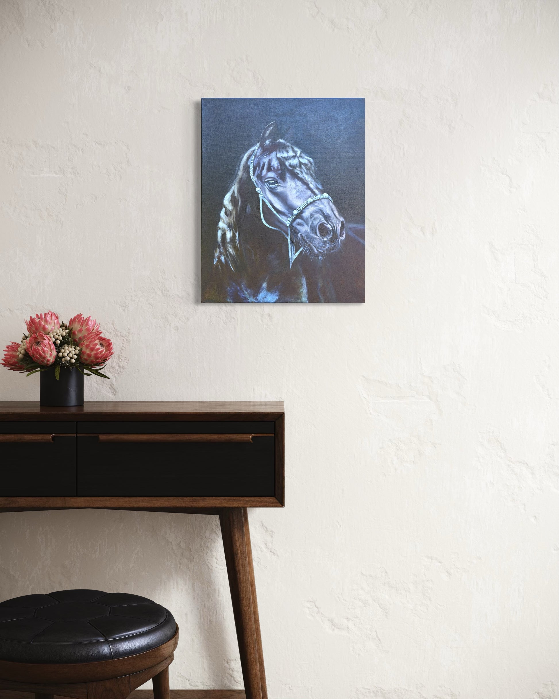 Painting of a black horse wearing a bridle hanging on a wall above a wooden desk with flowers.