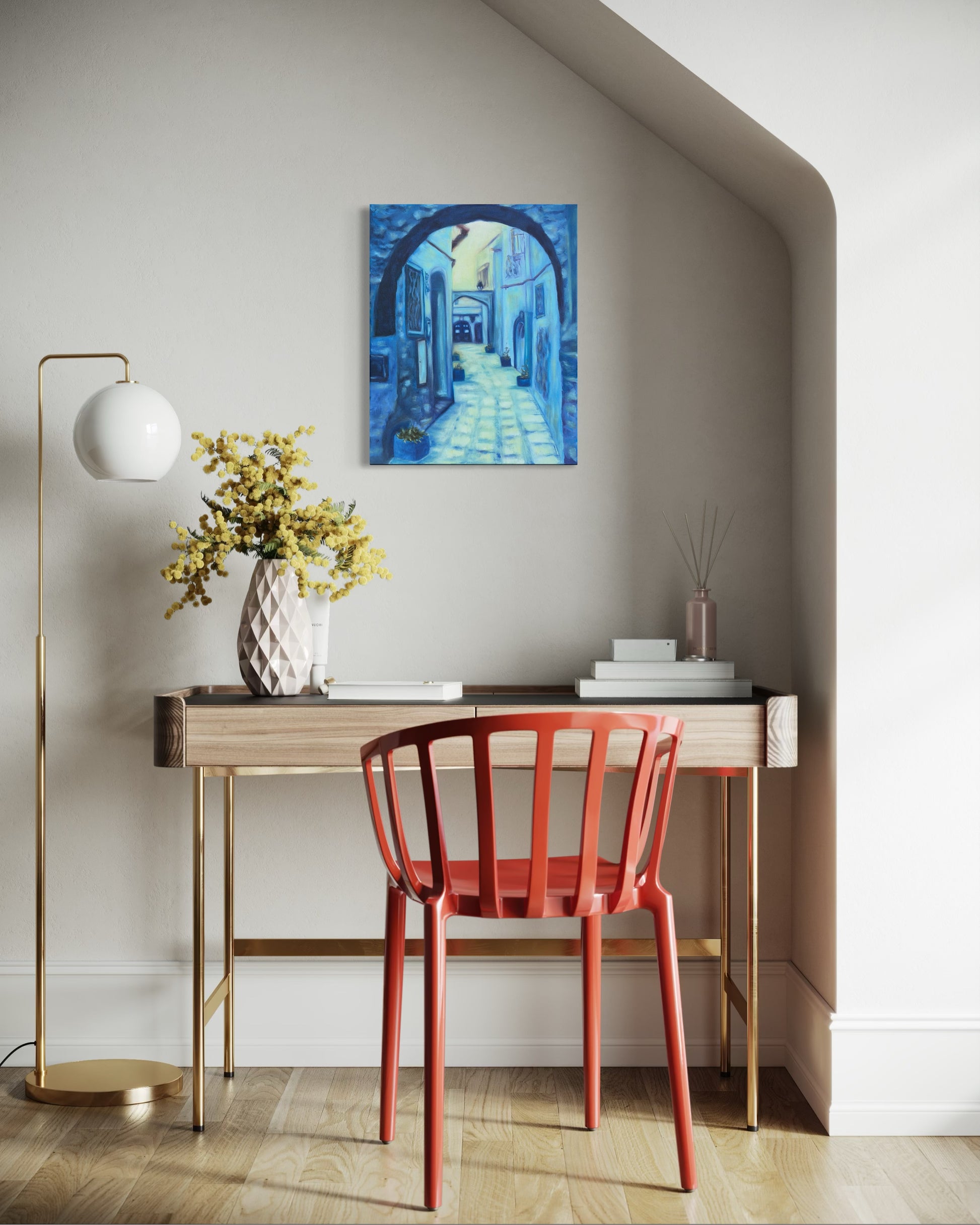 Modern interior with a red chair, wooden desk, and oil painting of a blue alleyway hanging on the wall.