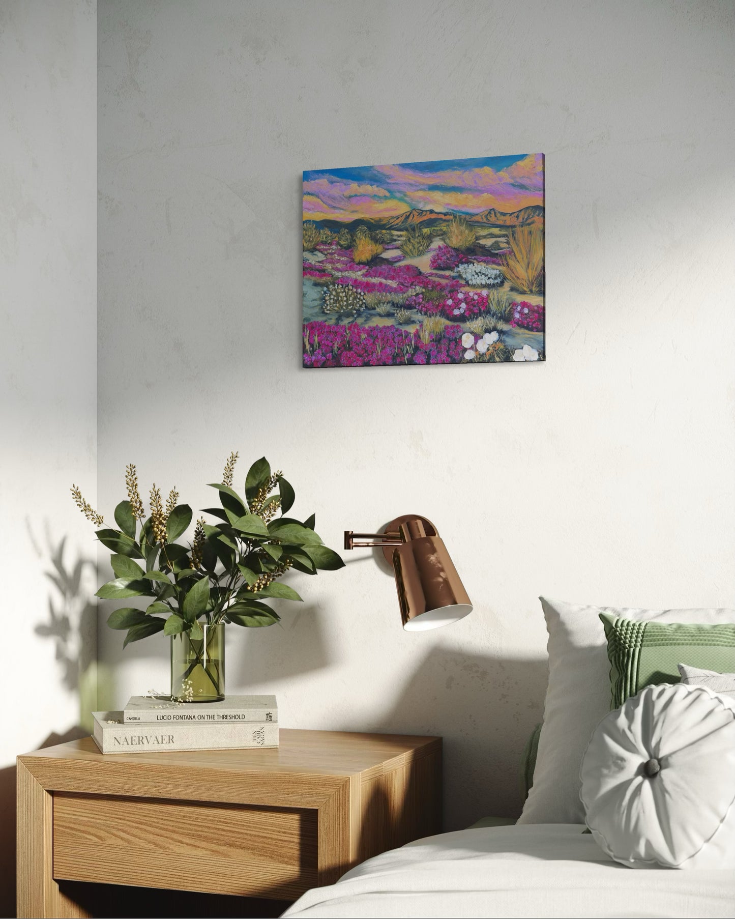 Decorative bedroom scene with an oil painting of a flowering desert landscape above a lamp and plants on a nightstand.