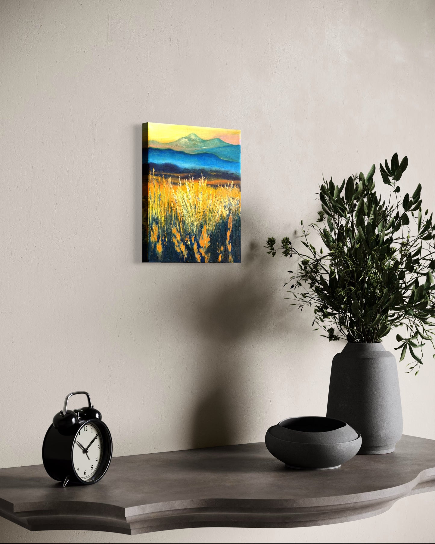 Oil painting of a landscape with faded mountains and fields of grass glowing from the sun hanging on a wall above a shelf with decorative items.