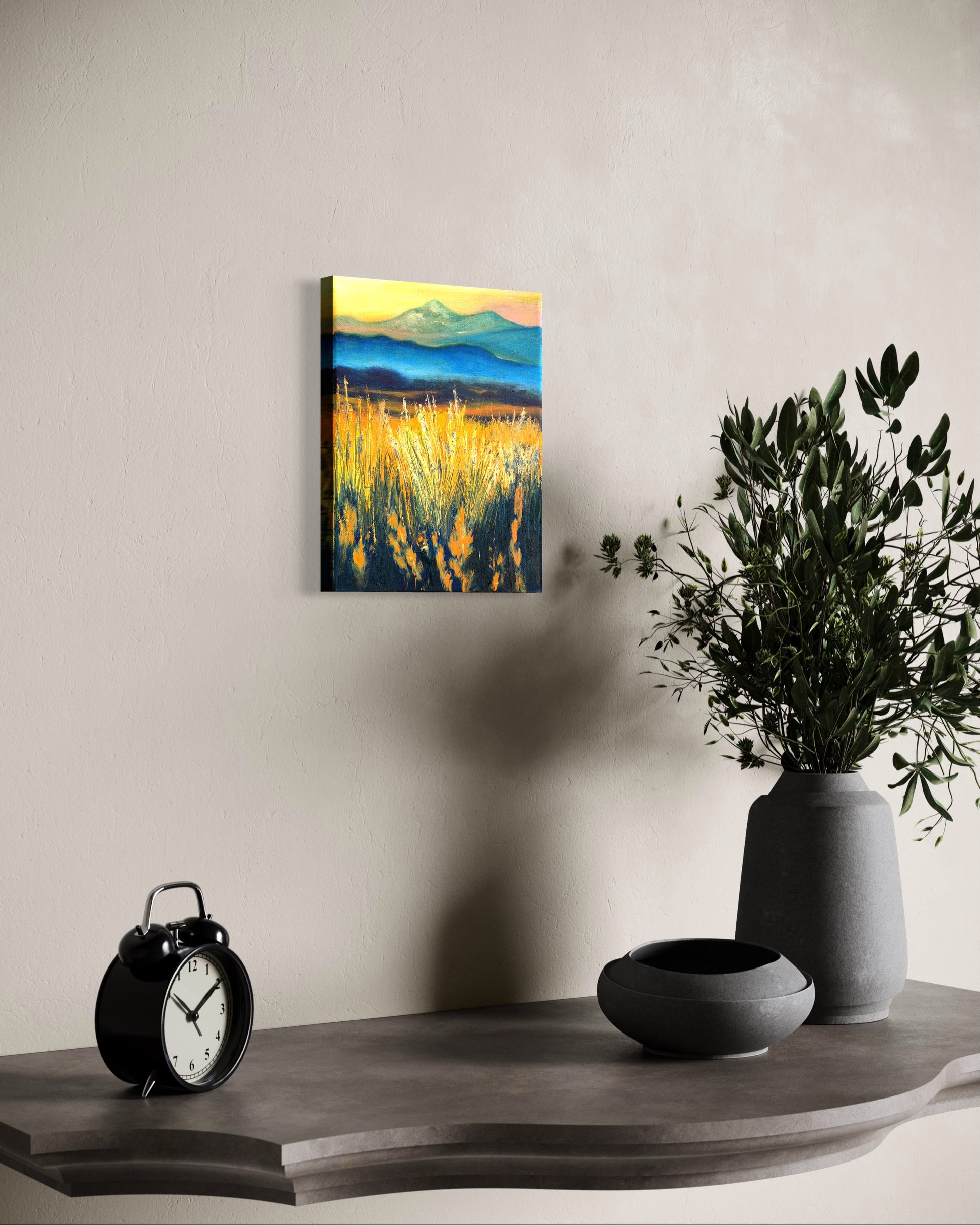 Oil painting of a landscape with faded mountains and fields of grass glowing from the sun hanging on a wall above a shelf with decorative items.