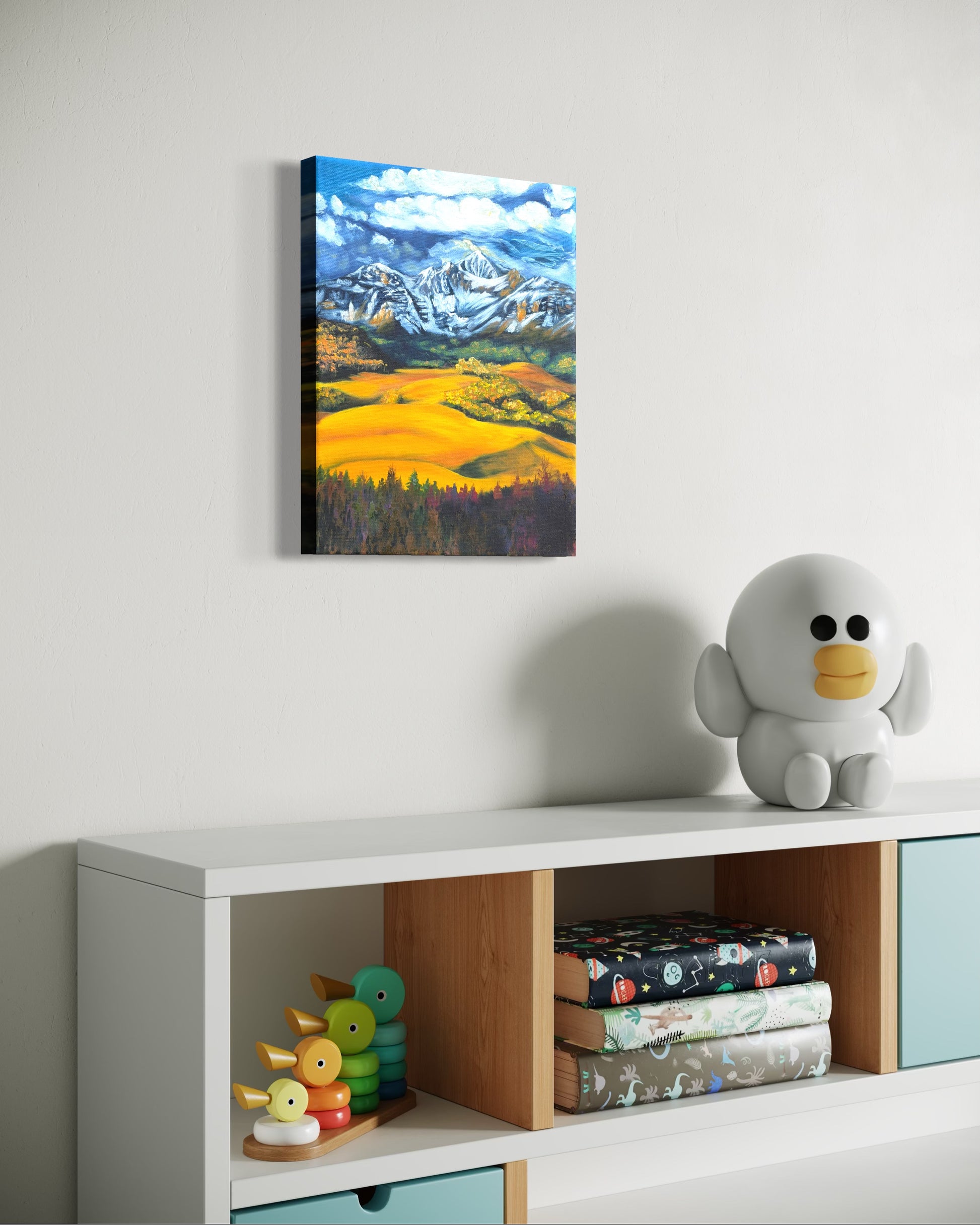 Oil painting of snow capped mountains and golden fields hanging on a wall above a shelf with toys and books.