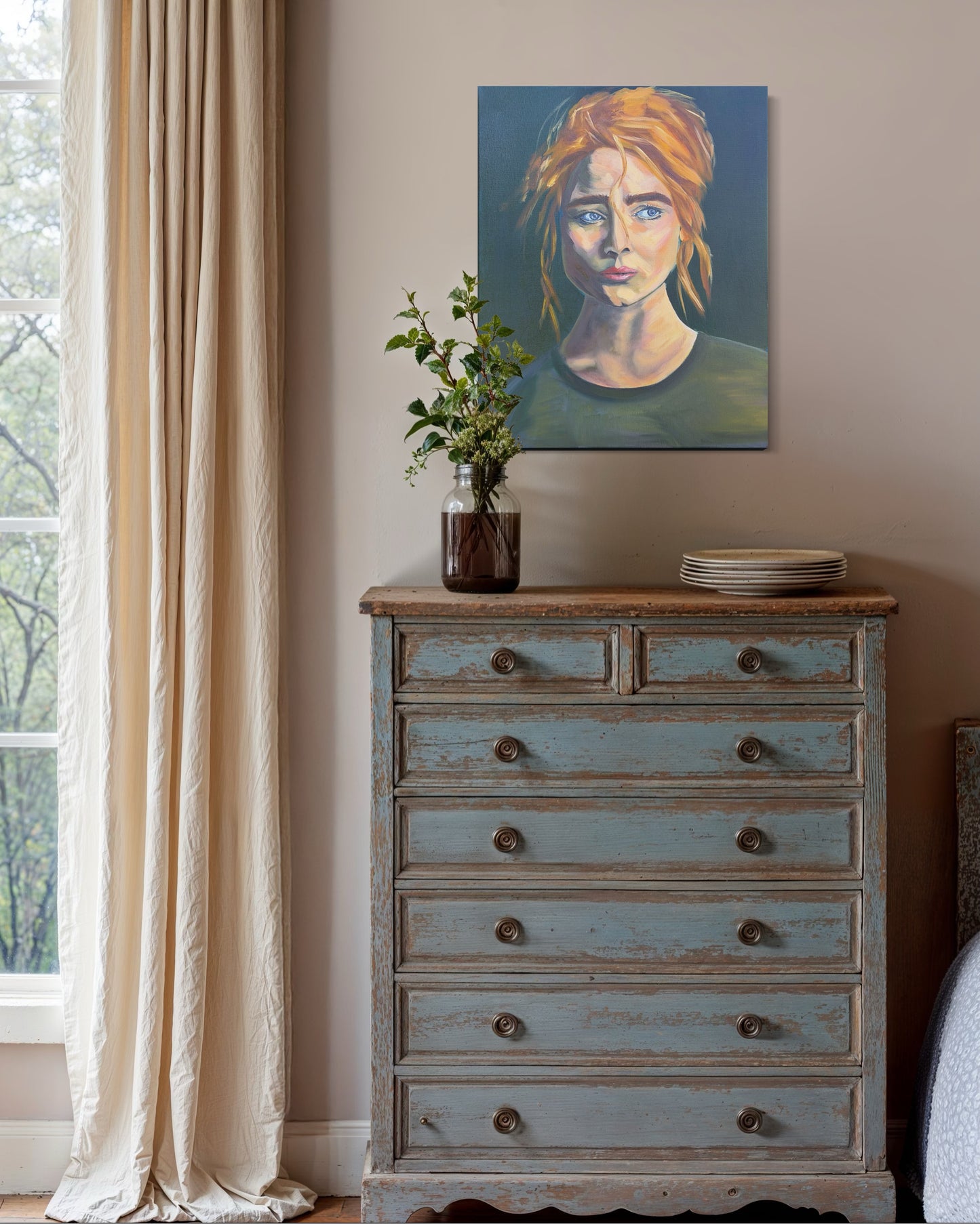 Vintage-style dresser with an oil painting of a woman's face above it, near a window with curtains.